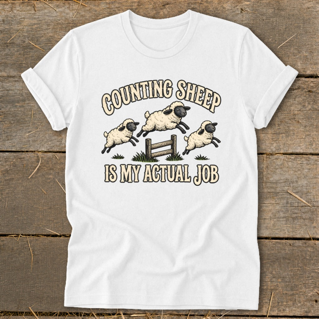 White t-shirt with "Counting Sheep Is My Actual Job" text and jumping sheep graphic.