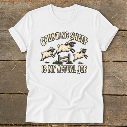 White t-shirt with "Counting Sheep Is My Actual Job" text and jumping sheep graphic.
