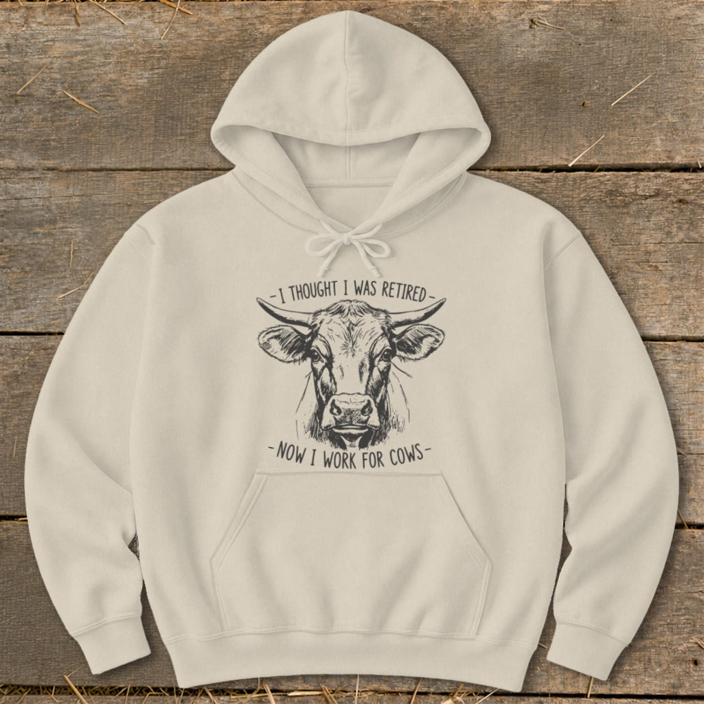 Cream hoodie with a sketched cow and text "I thought I was retired - now I work for cows".