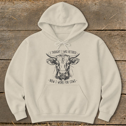 Cream hoodie with a sketched cow and text "I thought I was retired - now I work for cows".