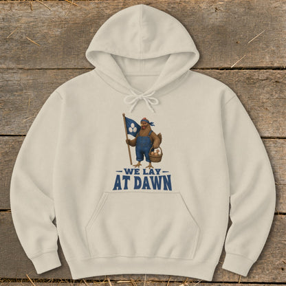 Cream hoodie with chicken graphic holding flag and eggs, text "WE LAY AT DAWN."