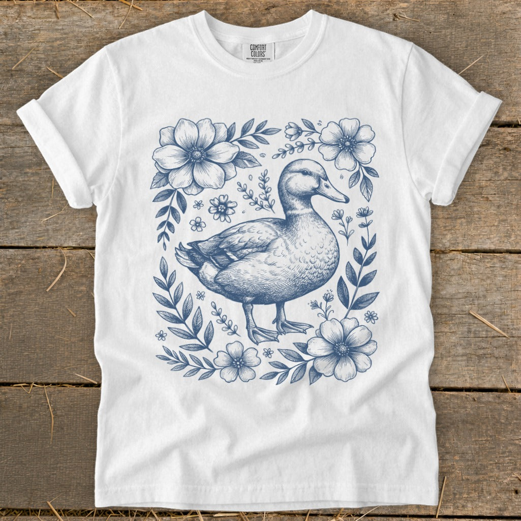 White t-shirt with a blue ink drawing of a duck surrounded by flowers.