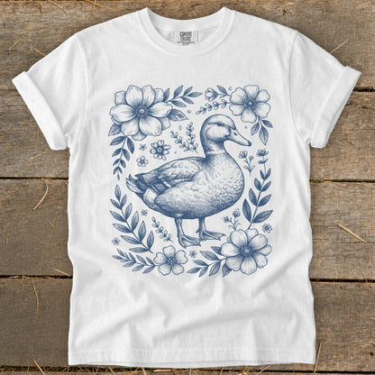 White t-shirt with a blue ink drawing of a duck surrounded by flowers.
