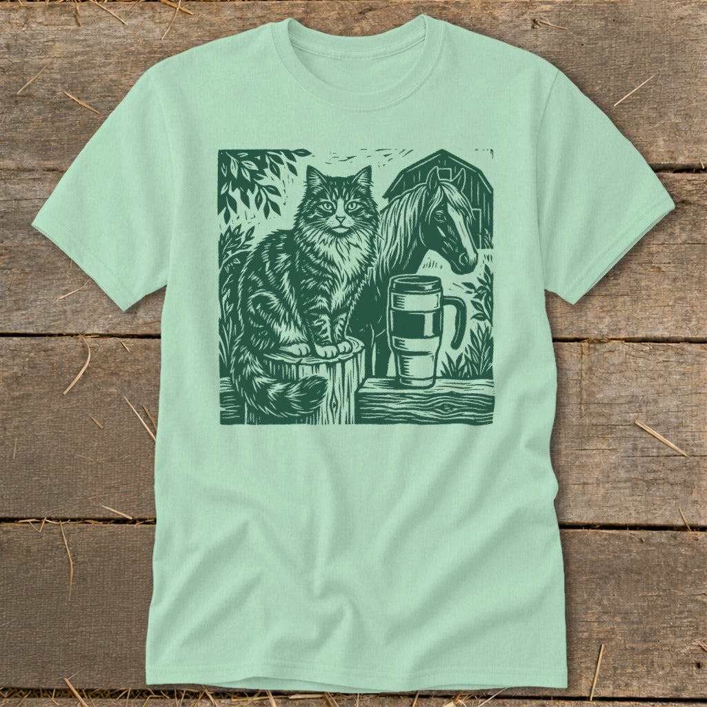 Green linocut print of cat, horse, mug, and barn on a mint t-shirt.