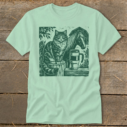 Green linocut print of cat, horse, mug, and barn on a mint t-shirt.