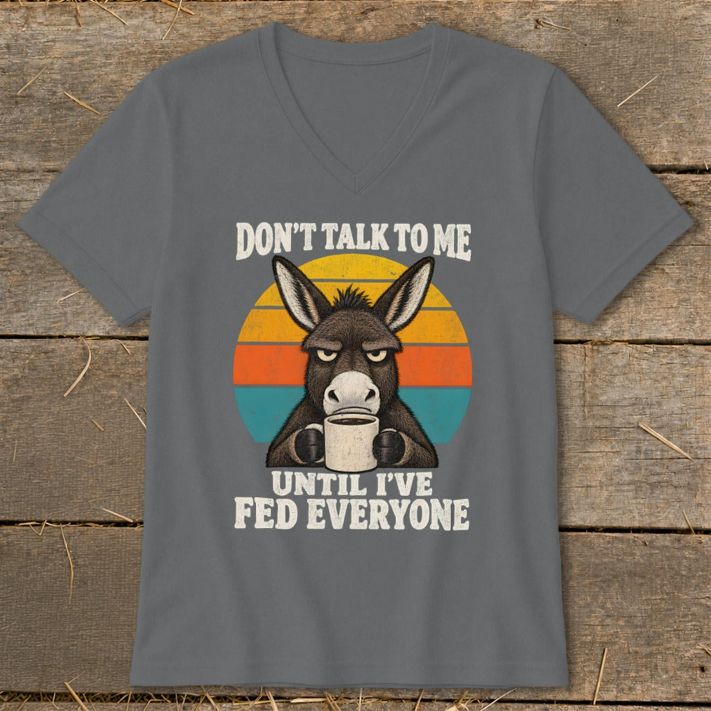 A dark gray V-neck t-shirt featuring a graphic of a grumpy donkey drinking coffee with the text "DON'T TALK TO ME UNTIL I'VE FED EVERYONE."