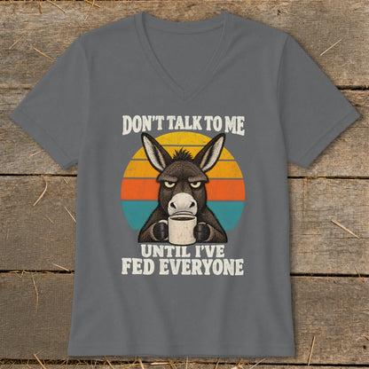 A dark gray V-neck t-shirt featuring a graphic of a grumpy donkey drinking coffee with the text "DON'T TALK TO ME UNTIL I'VE FED EVERYONE."
