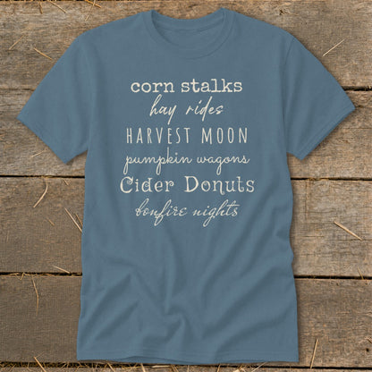 Blue t-shirt with white text listing fall activities: corn stalks, hay rides, harvest moon, pumpkin wagons, cider donuts, bonfire nights.