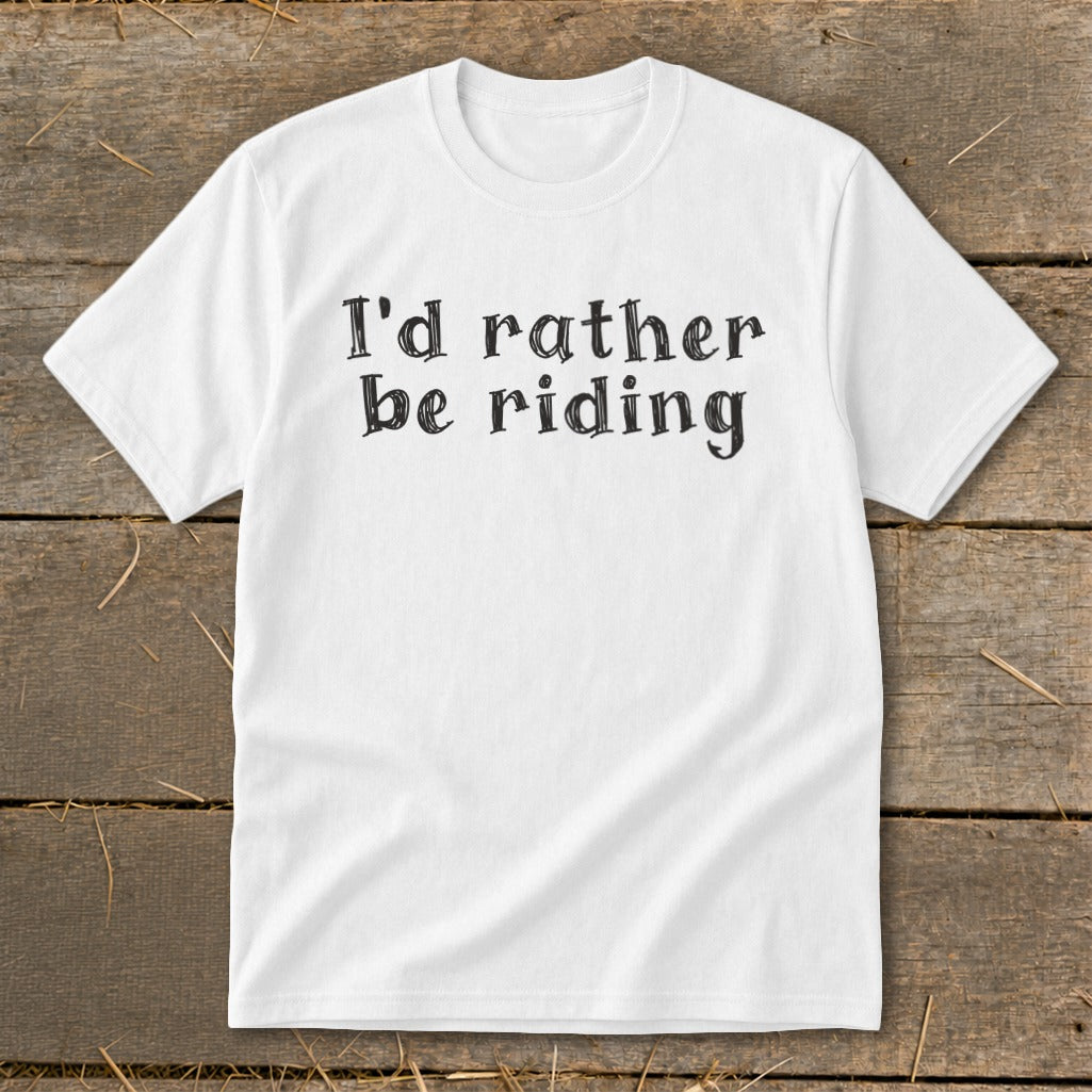 White t-shirt with black text "I'd rather be riding" on rustic wood.