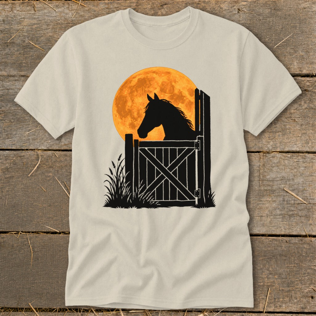A light-colored t-shirt with a black silhouette of a horse looking out a stable door over a large orange moon.