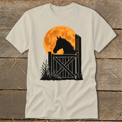 A light-colored t-shirt with a black silhouette of a horse looking out a stable door over a large orange moon.