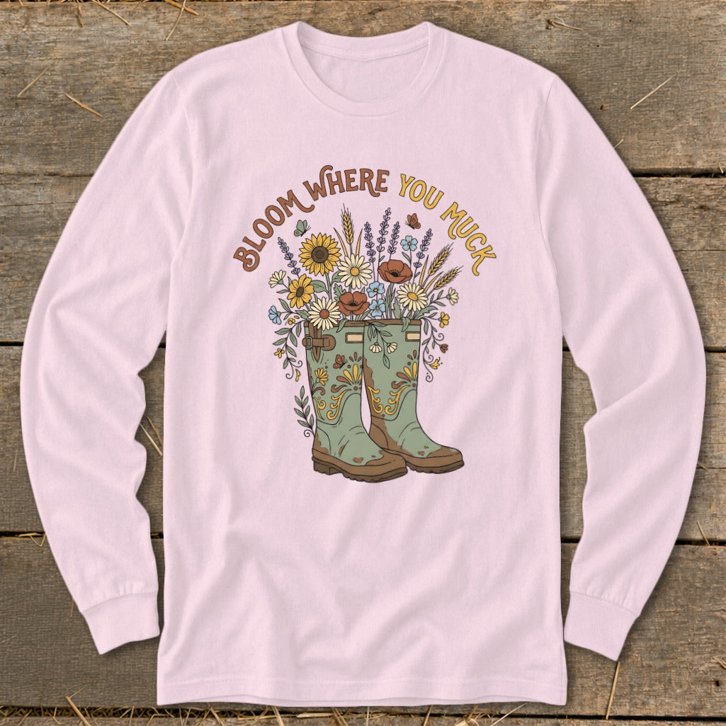 Pink long-sleeve shirt with green boots, flowers, and text "Bloom Where You Muck."