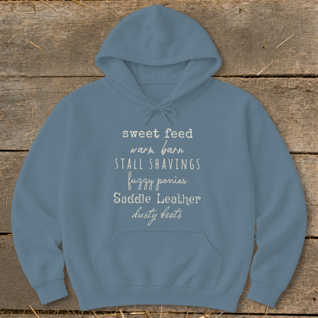 Blue hoodie with text: sweet feed, warm barn, stall shavings, fuzzy ponies, saddle leather, dusty boots.