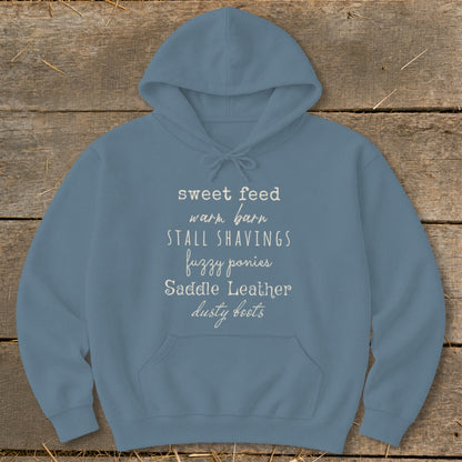 Blue hoodie with text: sweet feed, warm barn, stall shavings, fuzzy ponies, saddle leather, dusty boots.