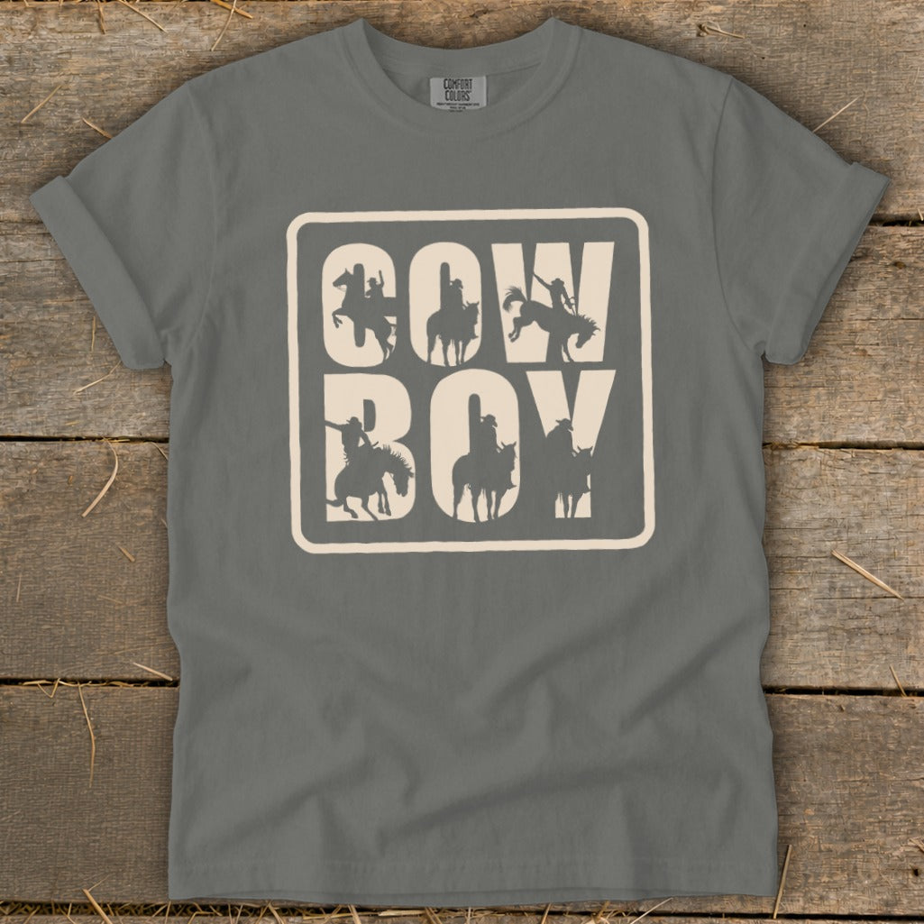 Grey t-shirt with "COW BOY" text and horse-riding silhouettes on a wooden background.