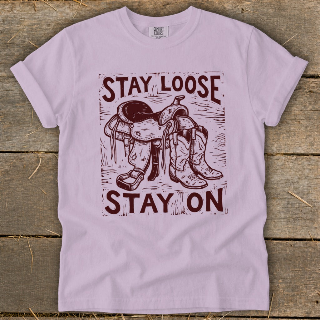 T-shirt with maroon graphic of a saddle and cowboy boots with text "STAY LOOSE STAY ON".