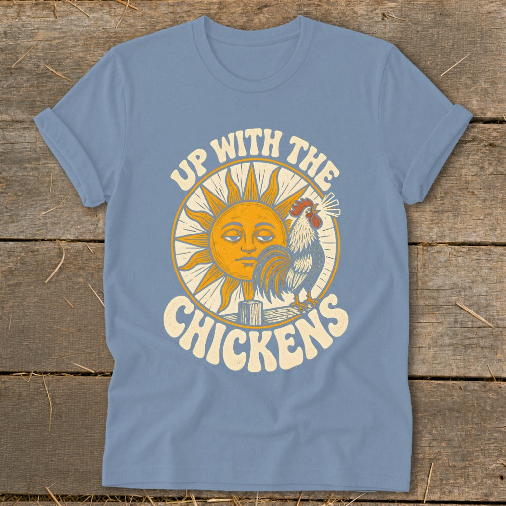 A dusty blue t-shirt printed with a graphic of a sun, a rooster, and the text Up With The Chickens.