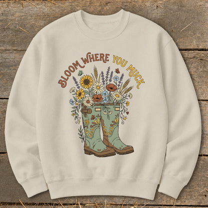 Cream sweatshirt with "Bloom Where You Muck" graphic of flowers in boots.