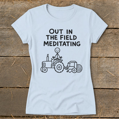 Light blue t-shirt with "Out in the field meditating" text and stick figure on tractor.