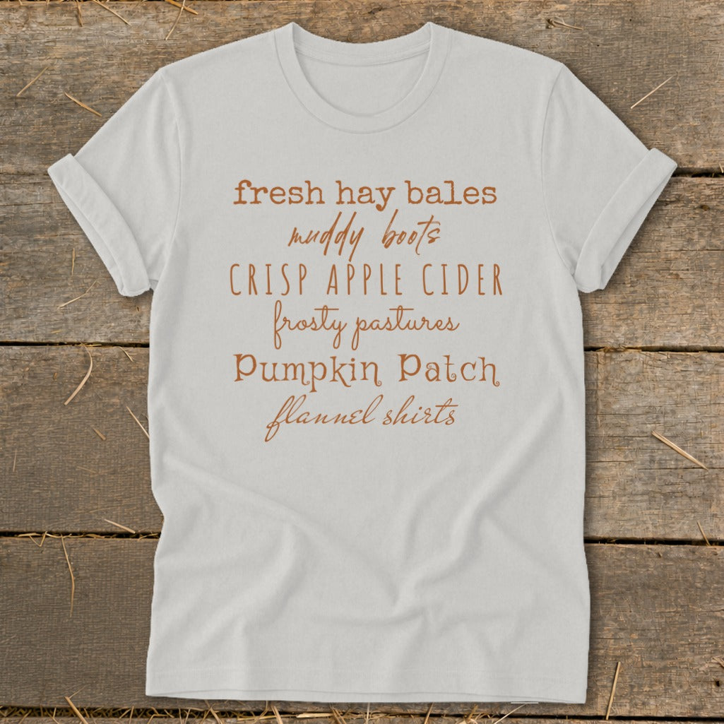 White t-shirt with autumn-themed text: fresh hay bales, muddy boots, crisp apple cider, frosty pastures, pumpkin patch, flannel shirts.
