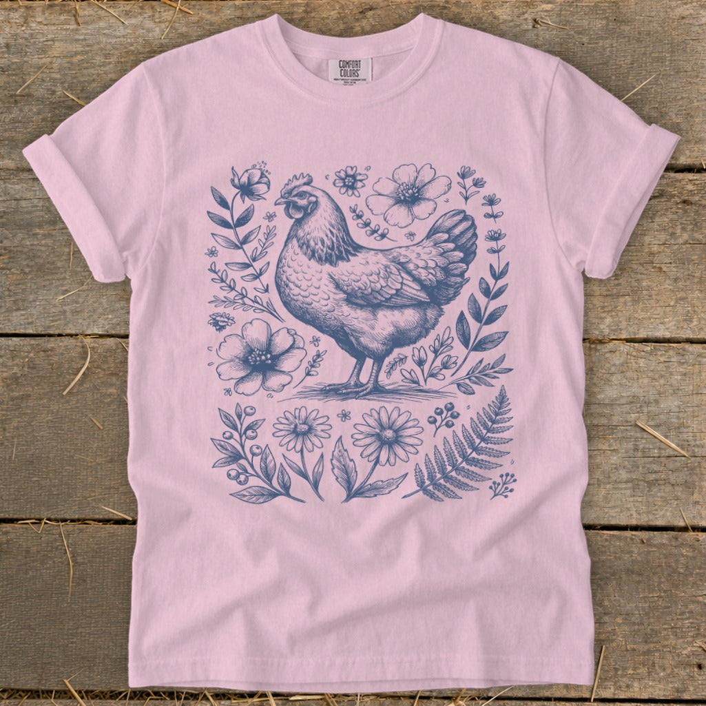Pink t-shirt with a blue ink sketch of a chicken surrounded by floral elements.