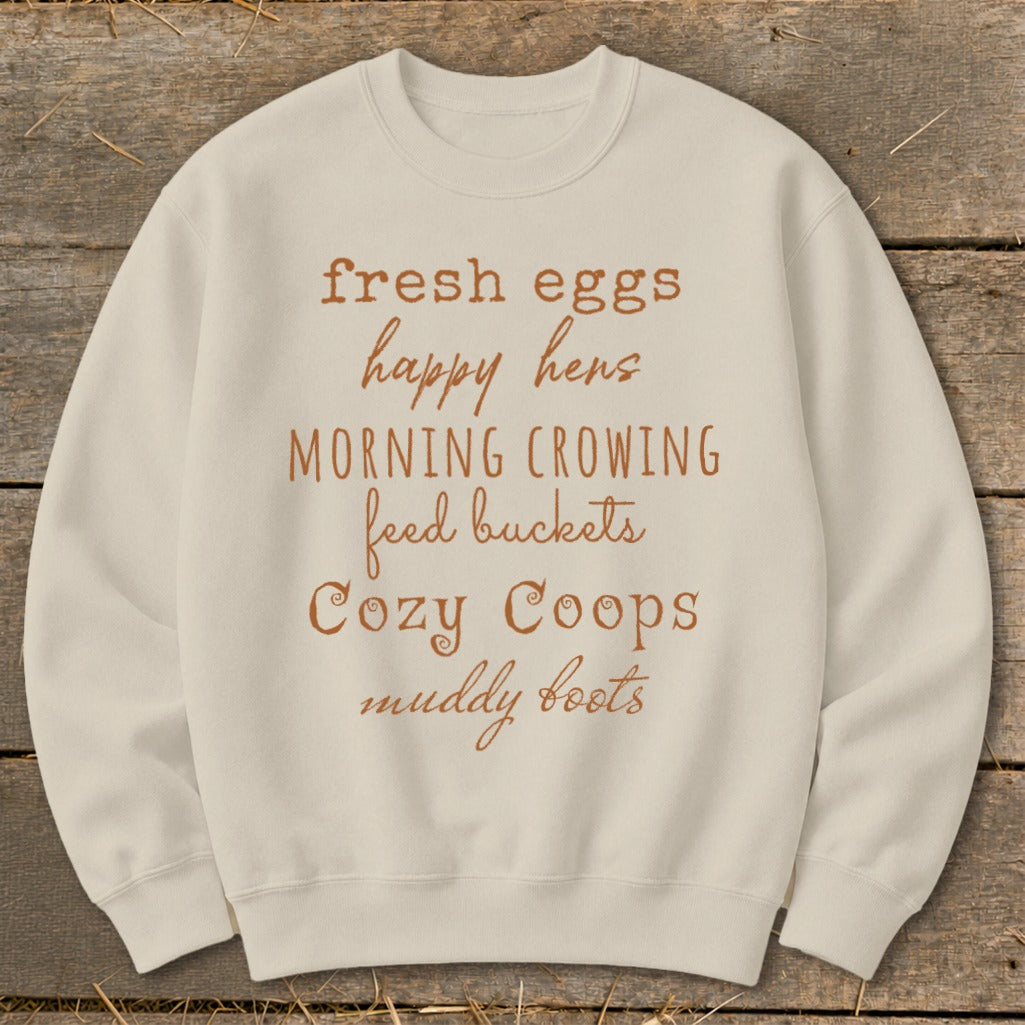 Cream sweatshirt with "fresh eggs happy hens morning crowing feed buckets cozy coops muddy boots" text.