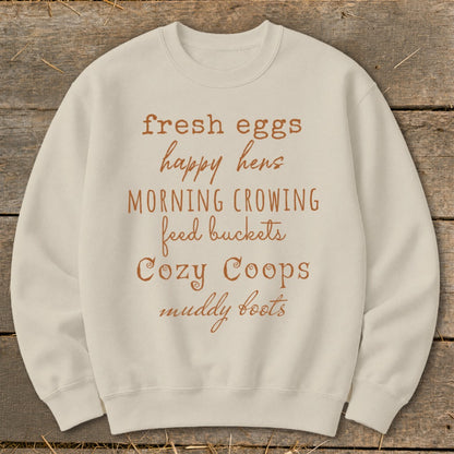 Cream sweatshirt with "fresh eggs happy hens morning crowing feed buckets cozy coops muddy boots" text.