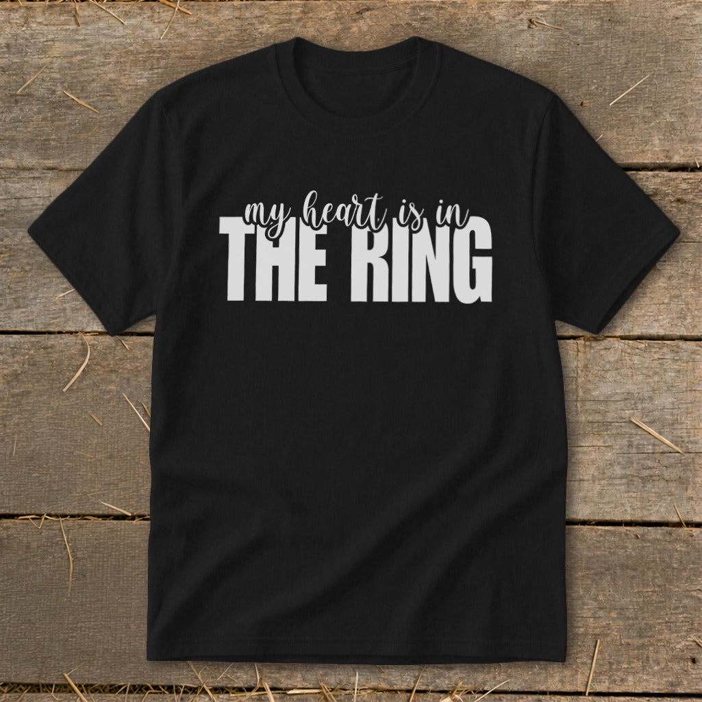 A black short-sleeved t-shirt with white text reading "my heart is in THE RING" centered on the chest, laid flat on a rustic wooden background.