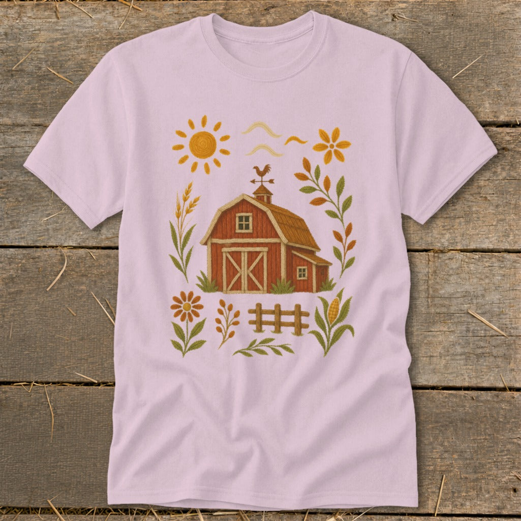 Pink t-shirt with embroidered barn, sun, fence, and farm elements.