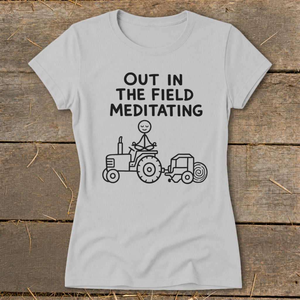 Light grey t-shirt with black text "OUT IN THE FIELD MEDITATING" and a stick figure meditating on a tractor.