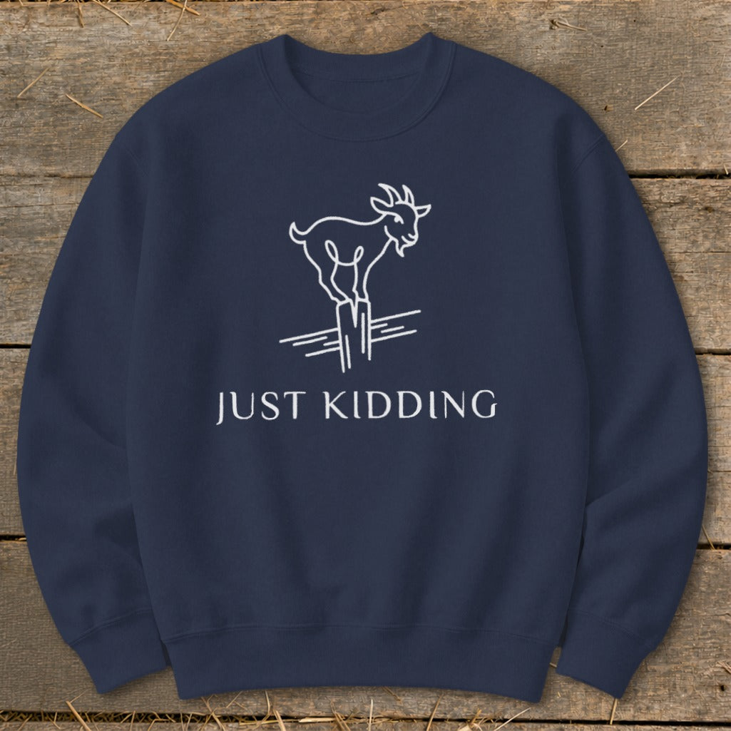 Navy sweatshirt with white line drawing of a goat on a post, text reads "JUST KIDDING".