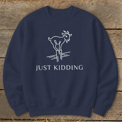 Navy sweatshirt with white line drawing of a goat on a post, text reads "JUST KIDDING".