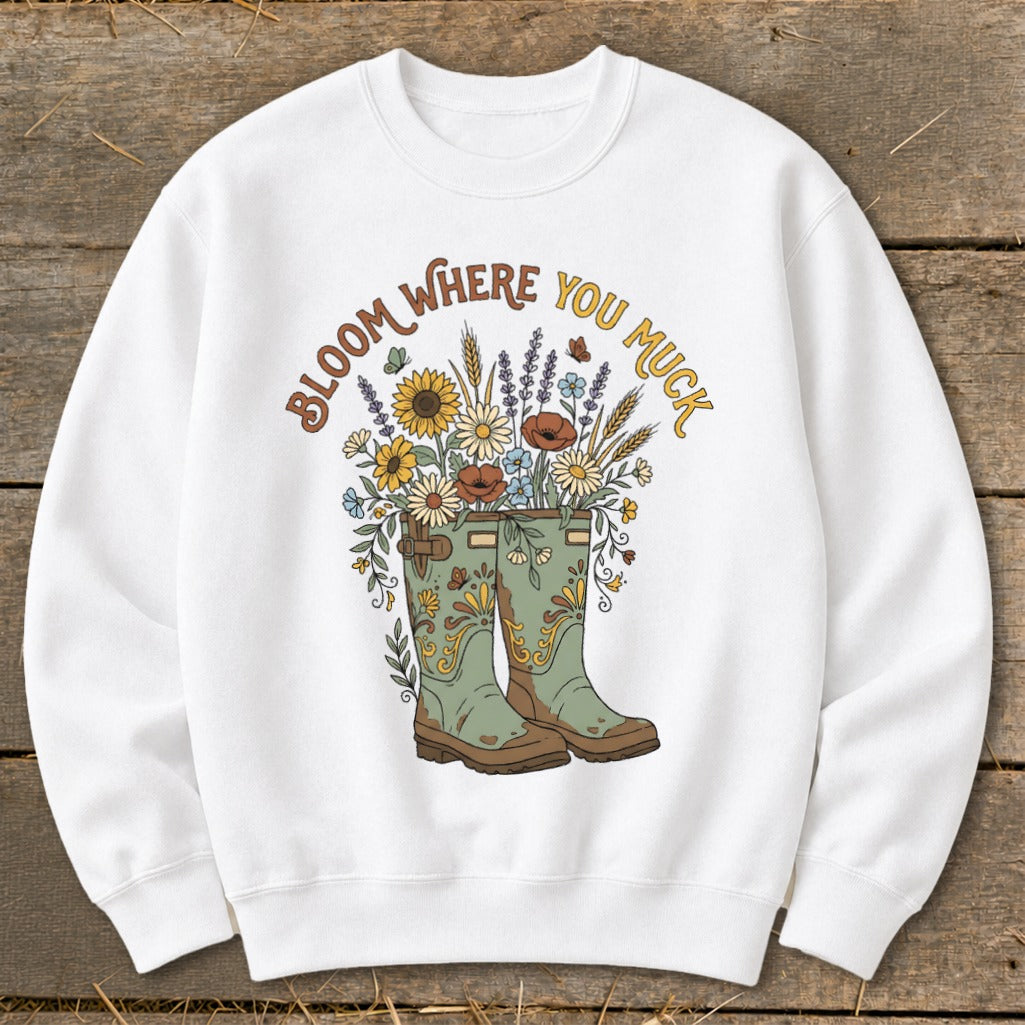 White sweatshirt with "Bloom Where You Muck" text and floral bouquet in boots.