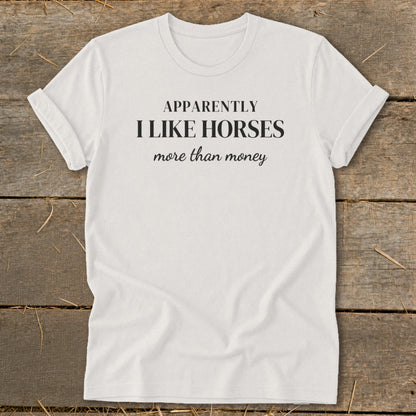 White t-shirt with black text: "APPARENTLY I LIKE HORSES more than money".