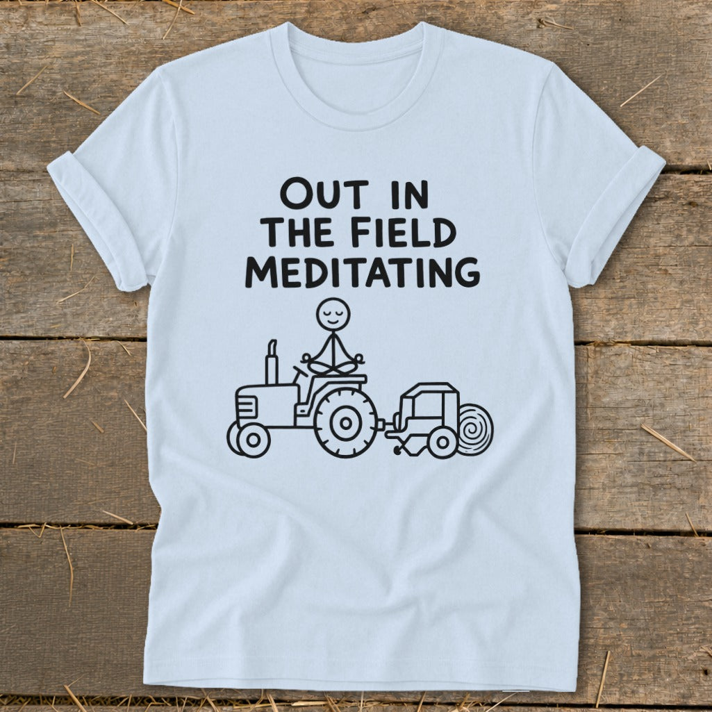 Light blue t-shirt with text "OUT IN THE FIELD MEDITATING" and a stick figure meditating on a tractor.