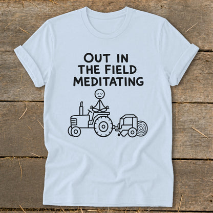 Light blue t-shirt with text "OUT IN THE FIELD MEDITATING" and a stick figure meditating on a tractor.
