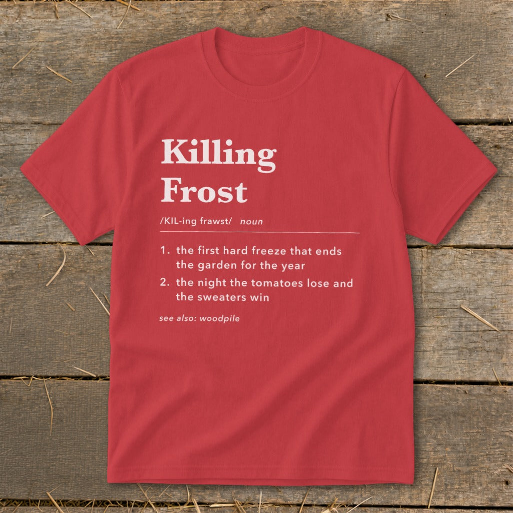 A red crewneck t-shirt rests on a wooden surface, printed with a humorous dictionary-style definition of Killing Frost.