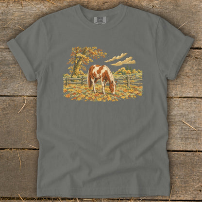 Brown and white horse grazing in a field of fall leaves near a wooden fence.