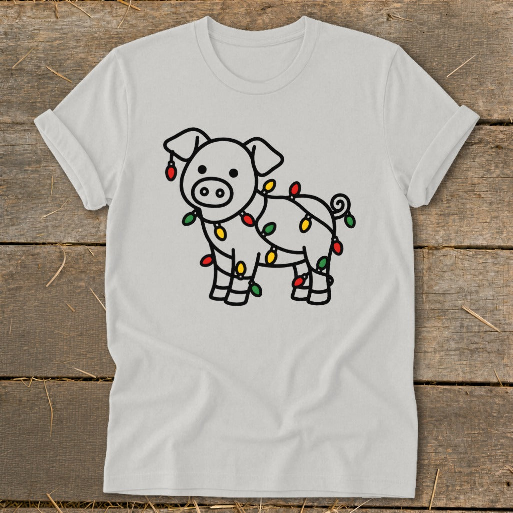 Light gray t-shirt featuring a cartoon pig wrapped in colorful Christmas lights, displayed on wood.