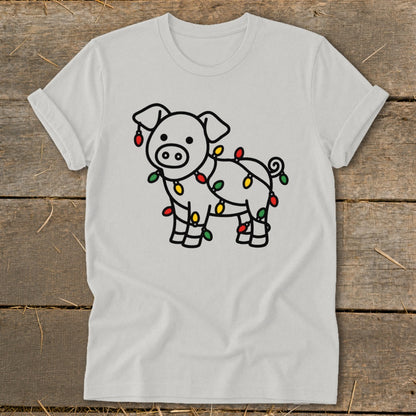Light gray t-shirt featuring a cartoon pig wrapped in colorful Christmas lights, displayed on wood.