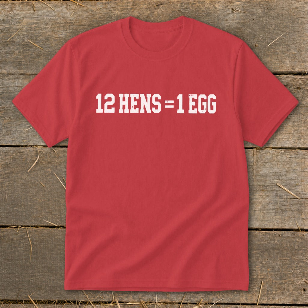 Red short-sleeved t-shirt with the white distressed text 12 HENS = 1 EGG on the chest, lying flat on a wooden background.