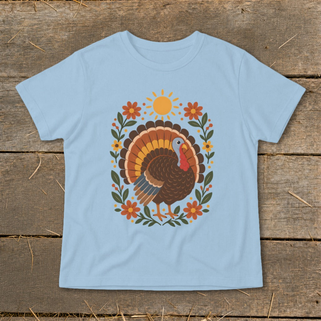 Light blue t-shirt with a cartoon turkey surrounded by flowers and a sun.