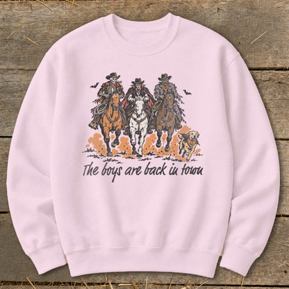 Pink sweatshirt with illustration of three skeletons riding horses and a dog, text reads "The boys are back in town".