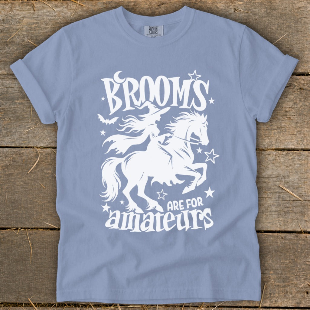 Light blue t-shirt with white graphic of witch on horse, text "Brooms are for amateurs."
