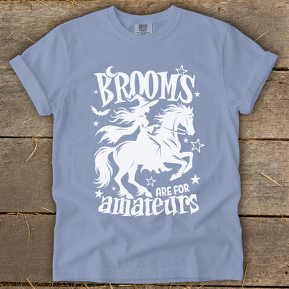 Light blue t-shirt with white graphic of witch on horse, text "Brooms are for amateurs."