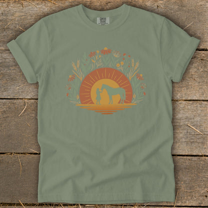 T-shirt with a graphic of a person and horse within a sun and floral border.