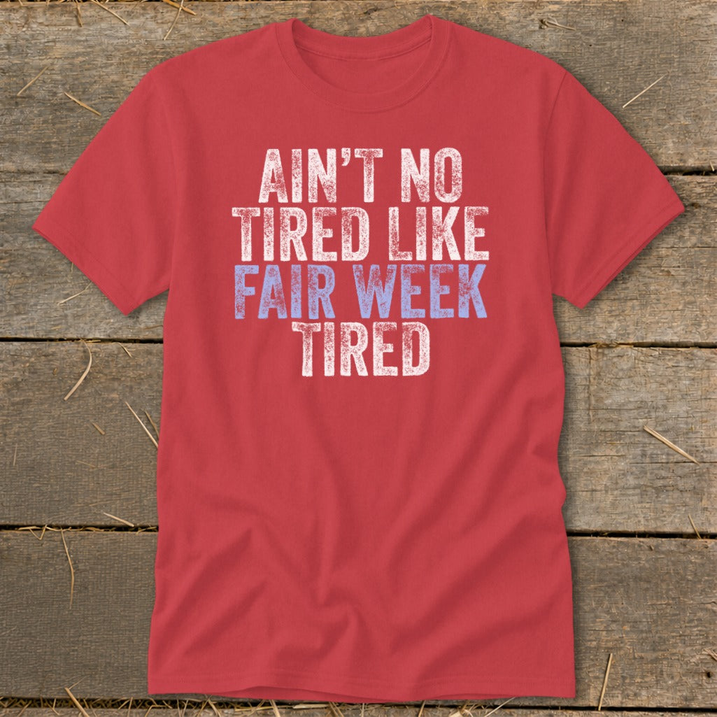 Red t-shirt with "AIN'T NO TIRED LIKE FAIR WEEK TIRED" graphic text.