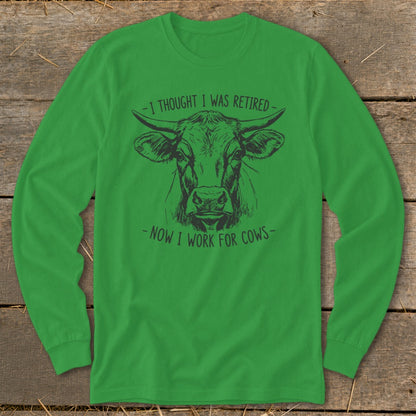 Green long-sleeve shirt with a cow graphic and text "-I THOUGHT I WAS RETIRED - NOW I WORK FOR COWS-".