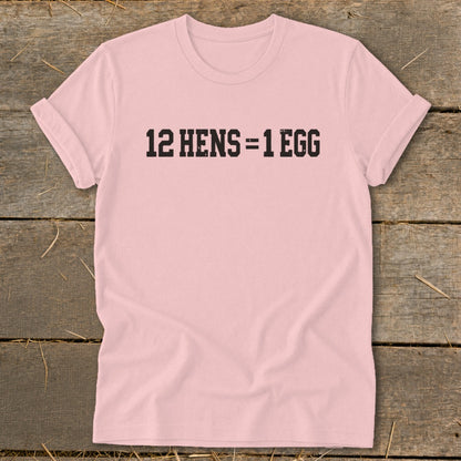 A light pink t-shirt with black text reading "12 HENS = 1 EGG" laid flat on wood.