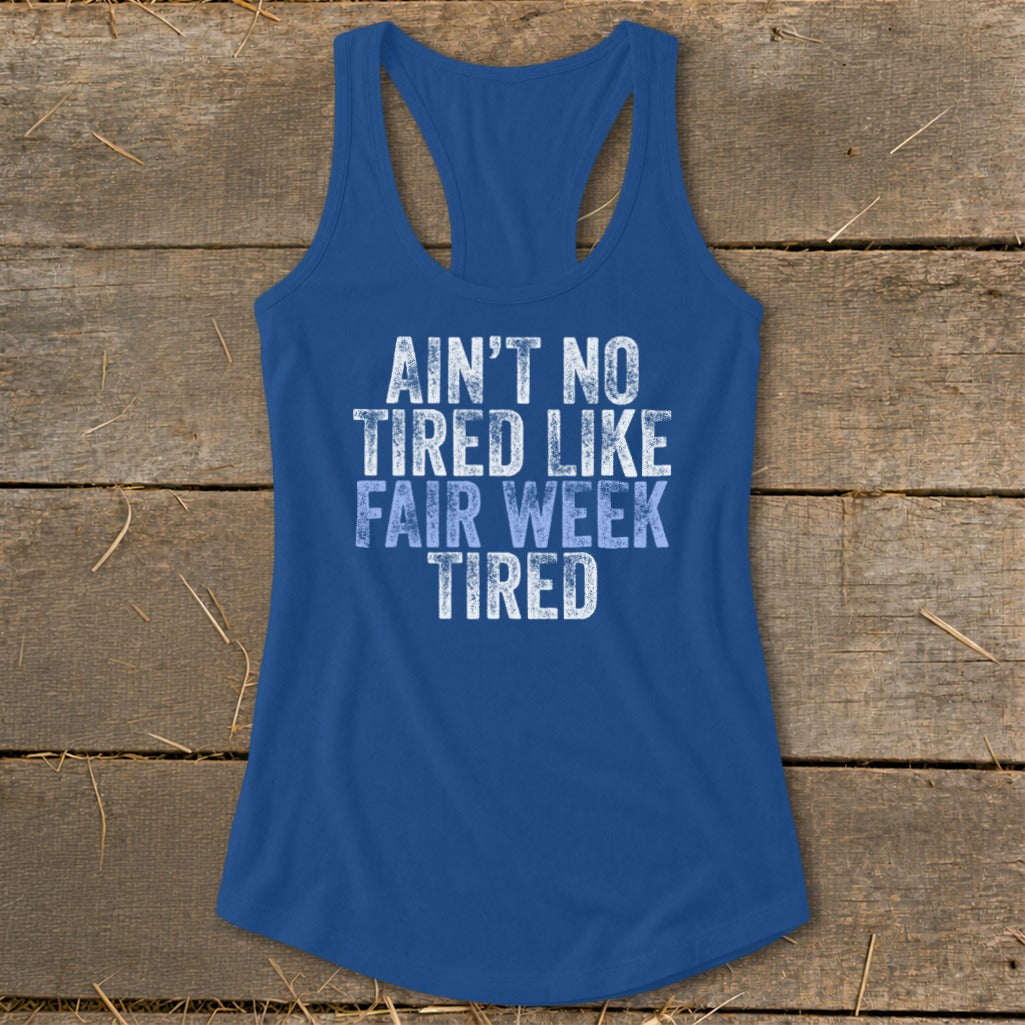 Blue racerback tank top with white text reading "Ain't No Tired Like Fair Week Tired".